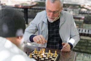 Senior companion caregiver playing chess outdoors with an older adult