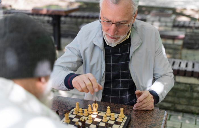 Senior companion caregiver playing chess outdoors with an older adult