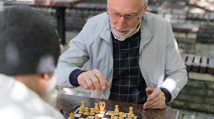 Senior companion caregiver playing chess outdoors with an older adult
