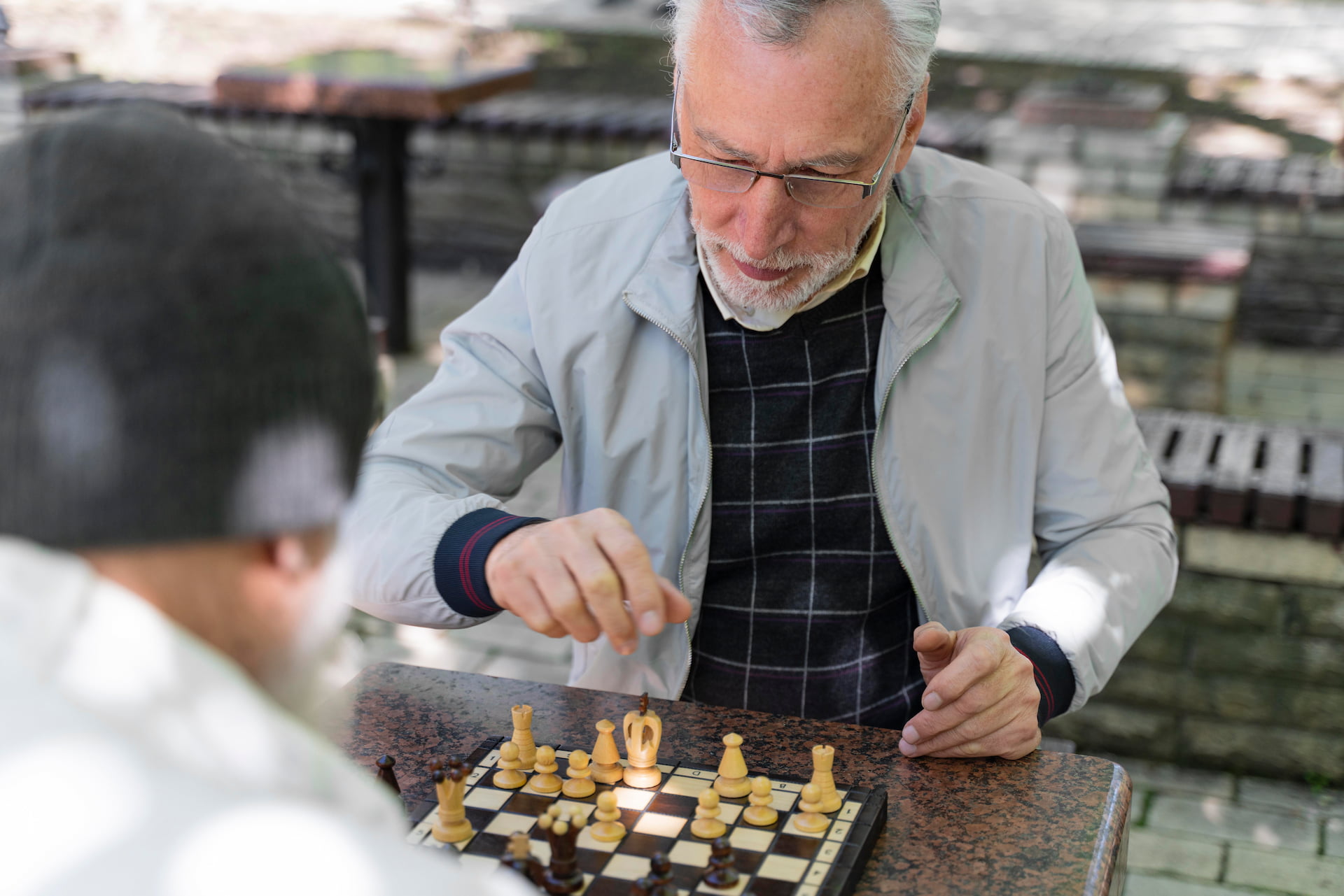 Senior companion caregiver playing chess outdoors with an older adult